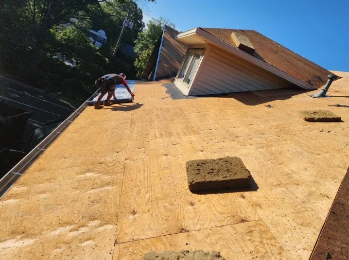 Roof replacement work showing exposed plywood decking before new shingles are installed.